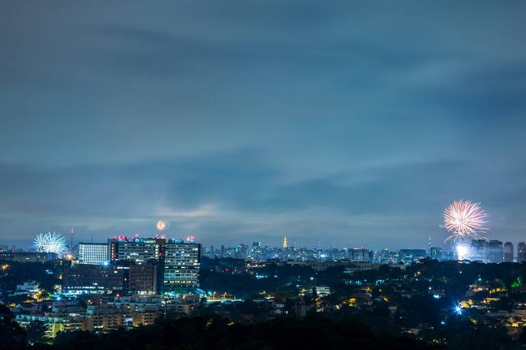 Vista panorâmica da cidade de São Paulo à noite, com fogos de artifício explodindo no céu, iluminando o horizonte urbano.