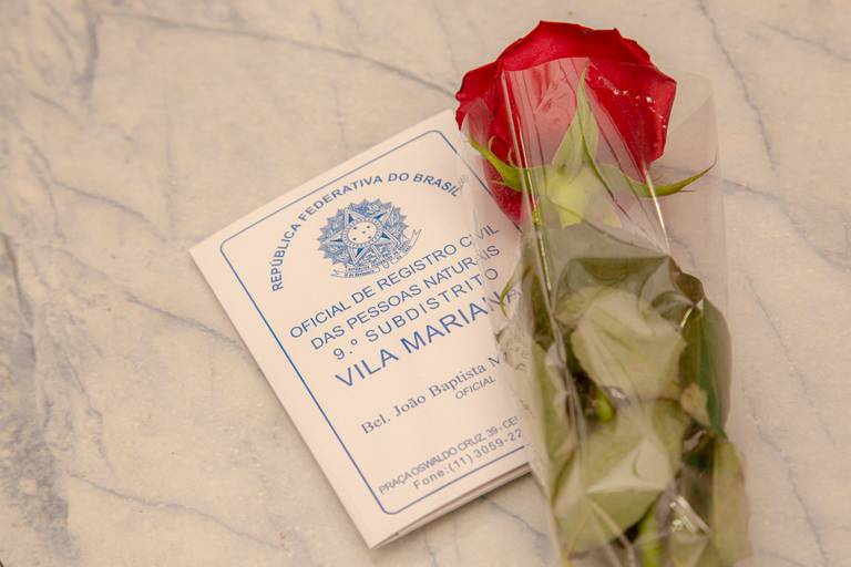 Detalhe da certidão de casamento em destaque, com uma flor delicada sobre ela, simbolizando a união.