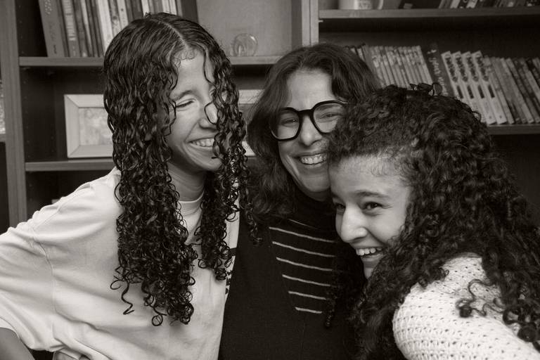 Mãe e suas duas filhas posando para uma foto, em um registro que destaca o vínculo familiar.