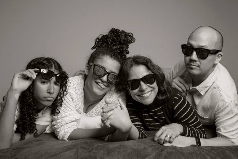 Quatro membros da família posando juntos para uma foto descontraída na cama, em um momento de união familiar.