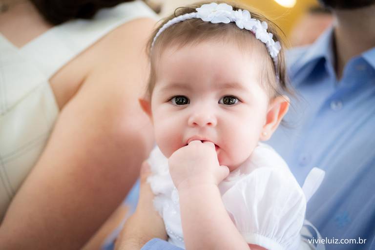 bebê de branco com a mão na boca