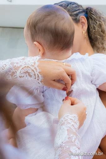 mãe arrumando a roupa da sua filha que irá ser batizada