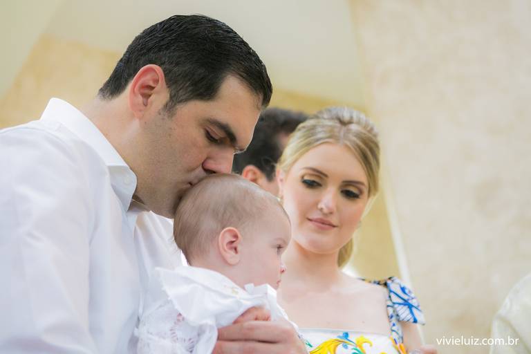 pai dando um beijo na cebeça do filho em seu batizado