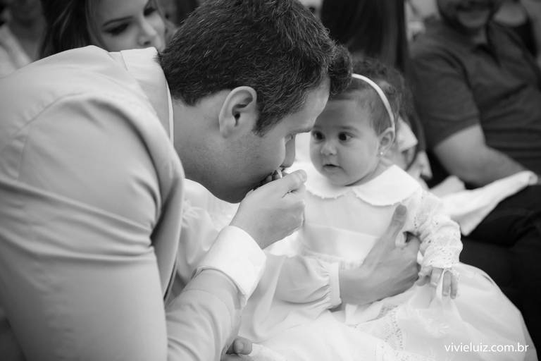 Pai dando um beijo na mão da filha no batizado dela
