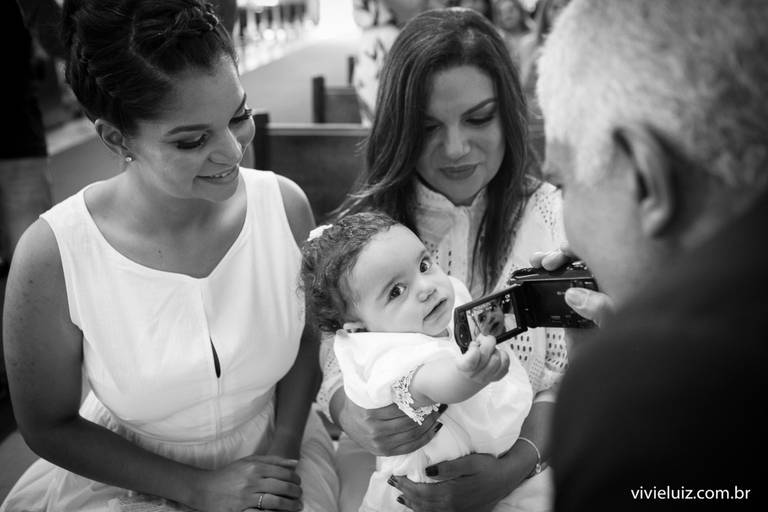 avô brincando com a neta e com uma câmera no batizado