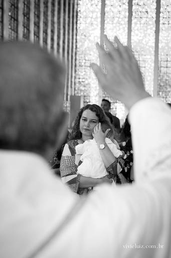 padre abençoando o bebê que está no colo da madrinha de batismo