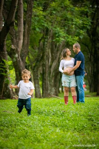 esposo segurando na barriga da esposa com o seu filho correndo a frente