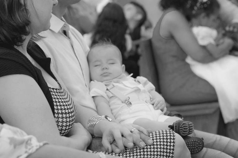 pais de mãos dadas com criança dormindo durante batizado na Paróquia São José, Osasco, São Paulo