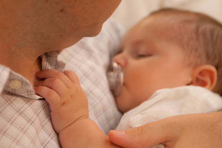 bebê dormindo no colo do pai durante batizado realizado na Paróquia São João Bosco, Americana, São Paulo