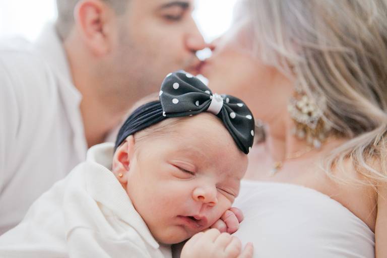 menina de laço no colo da mãe durante ensaio newborn, realizado na residência em Alphaville, Barueri, Osasco, São Paulo