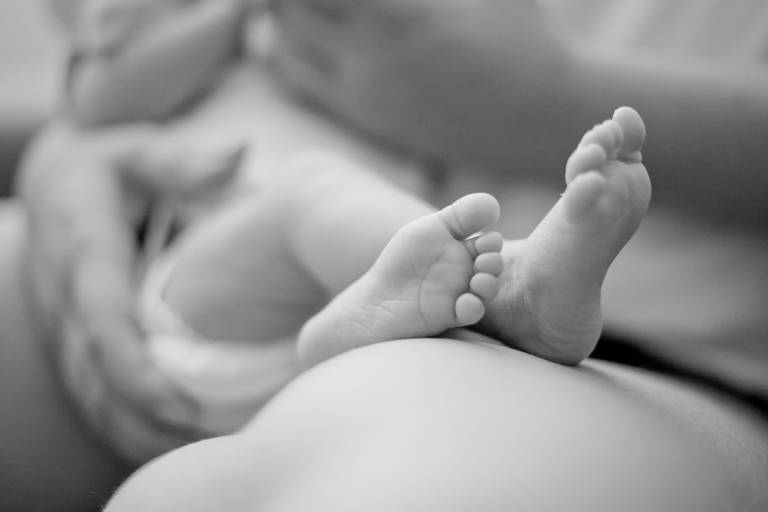 pé de bebê no colo da mãe durante ensaio newborn, realizado na residência em Alphaville, Barueri, Osasco, São Paulo, foto pb