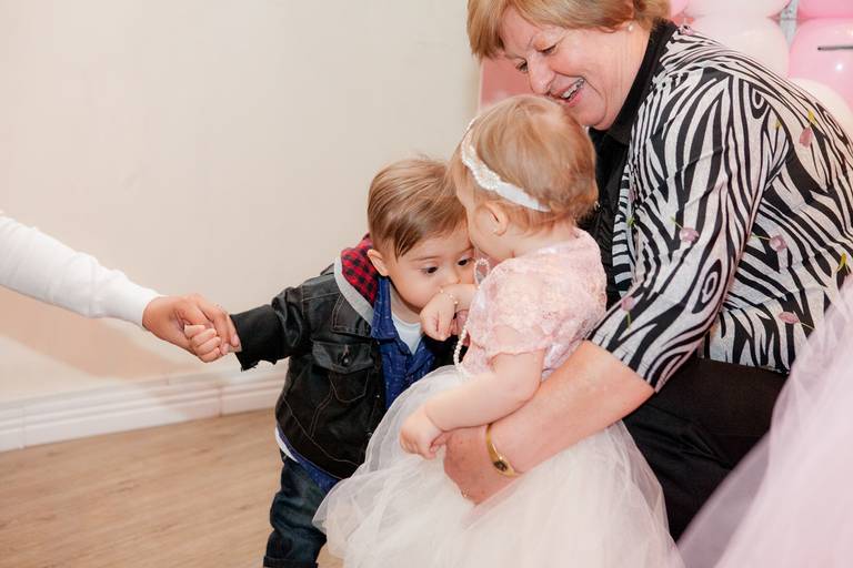 menina recebendo beijo na mão de amigo no colo da avó em sua festa de 1 aninho no Buffet Amazing, Alphaville, Barueri, São Paulo