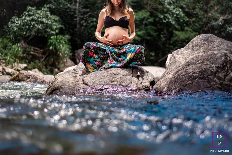 Fotografia de Gestante en Nova Friburgo - foto da gestante sentada de perna cruzada em uma pedra no curso de um rio