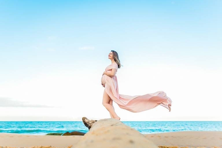 gestante com um vestido esvoaçante em pé em um tronco de árvore