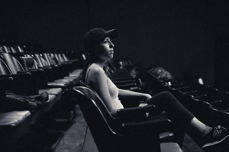 Menina sentada em plateia de teatro, garota sentada, mulher de perfil, garota de boné