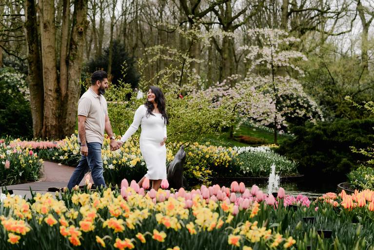 Couple walking through the flower paths of Keukenhof during a babymoon photography session, surrounded by tulips, daffodils, and blossoming trees. Perfect for visitors looking for a maternity photoshoot near Amsterdam.