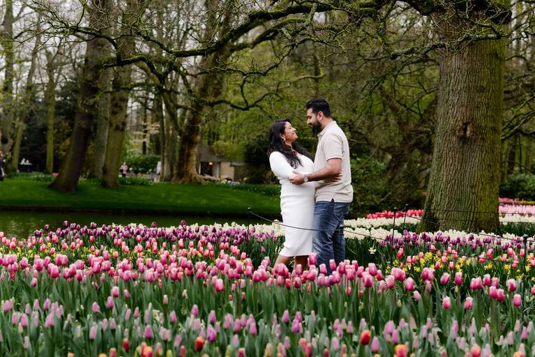 A couple enjoying a babymoon photoshoot at Keukenhof Gardens, standing between rows of pink and purple tulips. A popular day trip from Amsterdam for spring travelers who want maternity photos in the tulip fields of the Netherlands