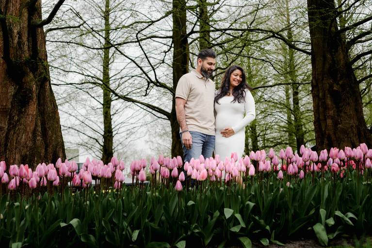 Babymoon photoshoot of an expecting couple looking at pink tulips in Keukenhof Gardens. A favourite experience for travelers visiting the Netherlands in spring who want tulip and maternity photography close to Amsterdam