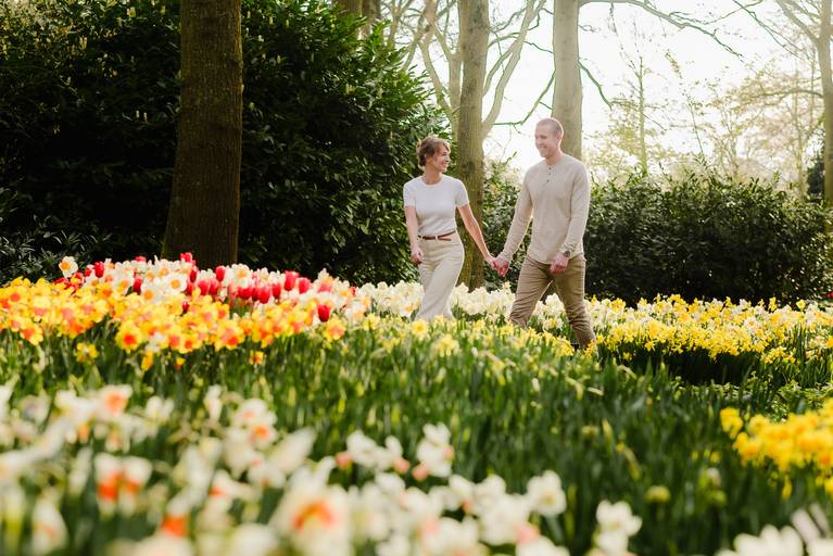 Couple holding hands and smiling while walking through pastel tulip beds at Keukenhof Gardens.