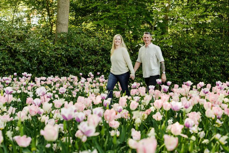 Smiling couple walking through pastel-colored tulips during a vacation photoshoot at Keukenhof Gardens. Ideal for travelers looking for spring photography experiences in the Netherlands