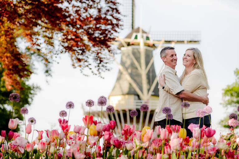 Couple embracing in front of the iconic windmill at Keukenhof Gardens, surrounded by pink tulips during a spring photoshoot. A popular activity for travelers visiting the Netherlands who want romantic vacation photos near Amsterdam.