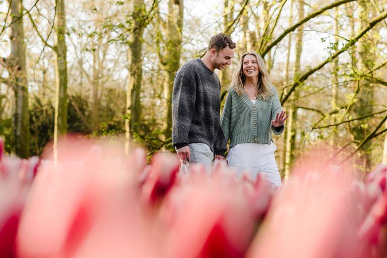 Couple walking through tulips in Keukenhof after their engagement. She admires her ring as they enjoy a quiet path. Created by a photographer experienced in guiding surprise proposals to hidden, crowd-free spots.