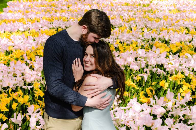 Just-engaged couple embracing in Keukenhof Gardens, surrounded by soft pink and yellow tulips. Captured right after a surprise proposal in a quiet area I guide clients to for crowd-free backgrounds