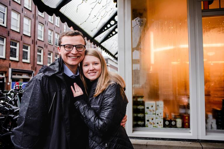 Happy couple posing on a rainy Amsterdam street, showing the charm of winter engagement photos in the city.