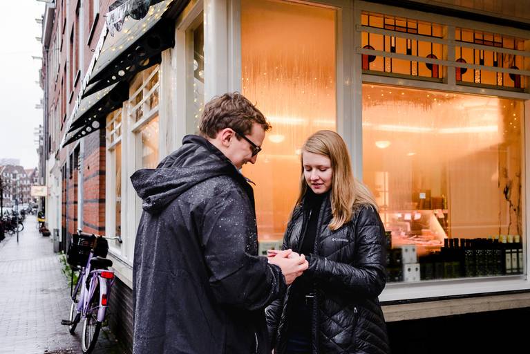 Newly engaged couple admiring the ring outside a glowing Amsterdam shop, ideal inspiration for intimate proposal photos in the city.