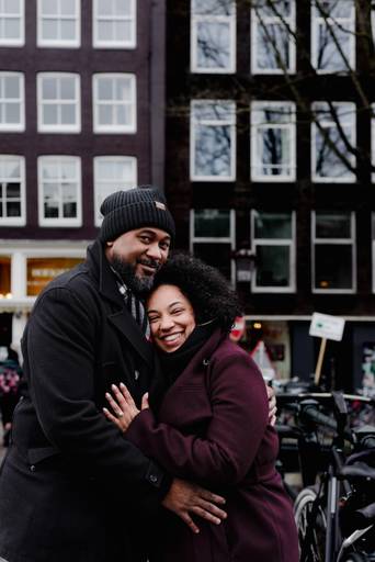 Couple hugging and smiling on an Amsterdam canal bridge, great example of relaxed couple photos for visitors wanting portraits during their trip.