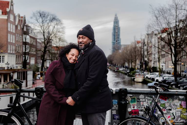 Couple embracing on an Amsterdam canal bridge, warm and intimate portrait for travelers wanting romantic photos during their visit to the city.