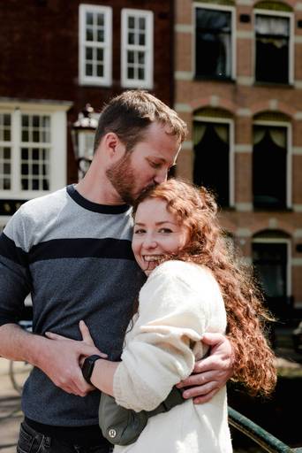 Close-up of a couple hugging on an Amsterdam bridge as he kisses her forehead, part of their engagement session.