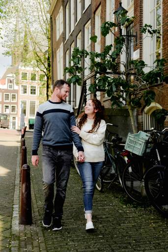 Couple walking hand in hand along a peaceful Amsterdam street lined with historic canal houses.
