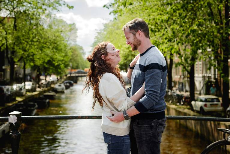 Couple laughing together on an Amsterdam bridge with canal water behind them, captured during an engagement session.