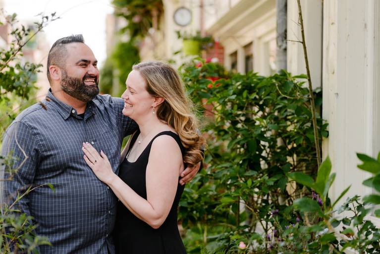 Laughing couple in a small Amsterdam street surrounded by plants and historic homes during their engagement shoot.