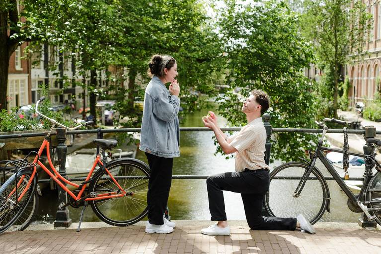 Surprise proposal on an Amsterdam canal bridge, with one partner kneeling and the other reacting with joy during a private moment.