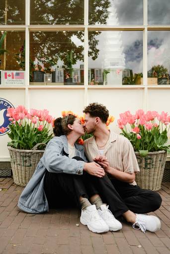 Engaged couple kissing in front of bright tulips outside a flower shop in Amsterdam, sharing a sweet moment after the proposal.