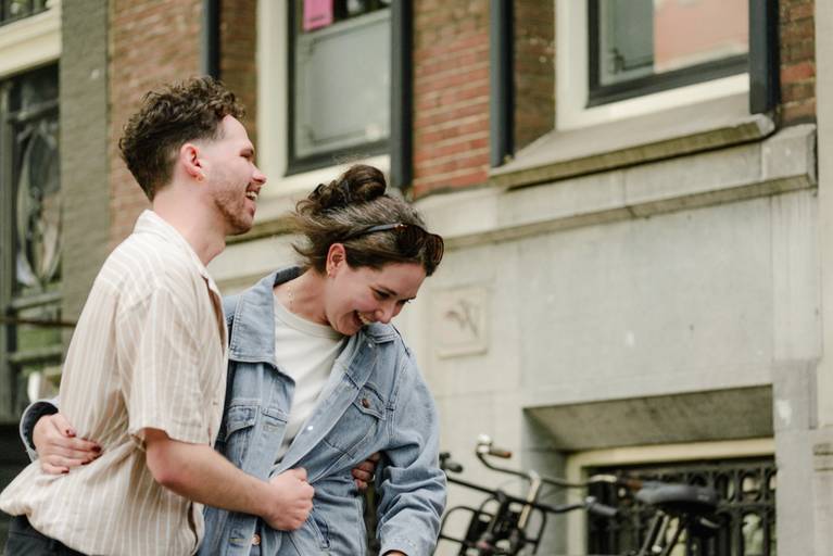 Candid moment of an engaged couple laughing together during a proposal photoshoot on an Amsterdam street.