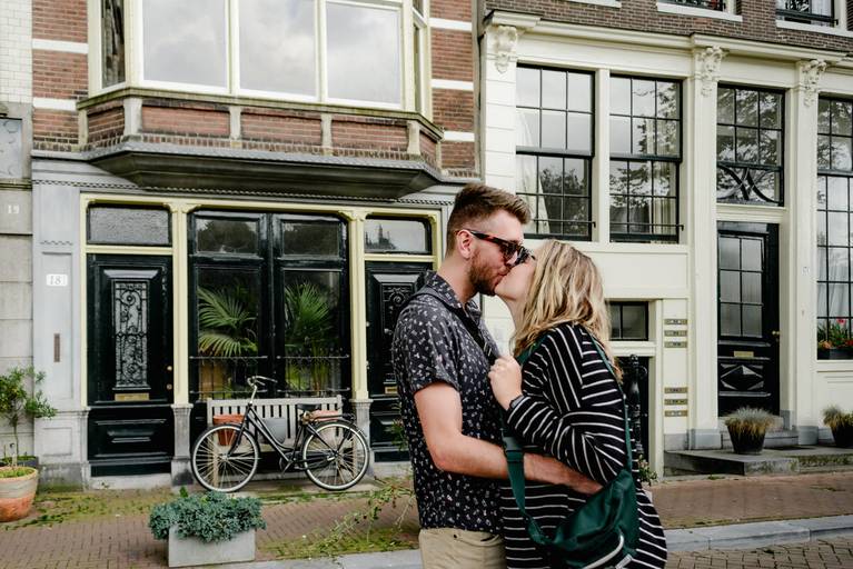 Couple kissing in front of historic Amsterdam houses with a parked bicycle during their engagement photo session.
