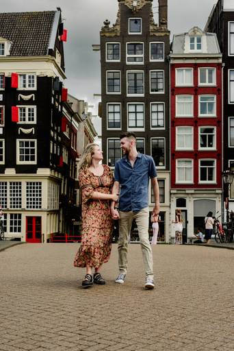 Couple walking hand in hand on a bridge in Amsterdam, framed by traditional Dutch houses during a proposal session.