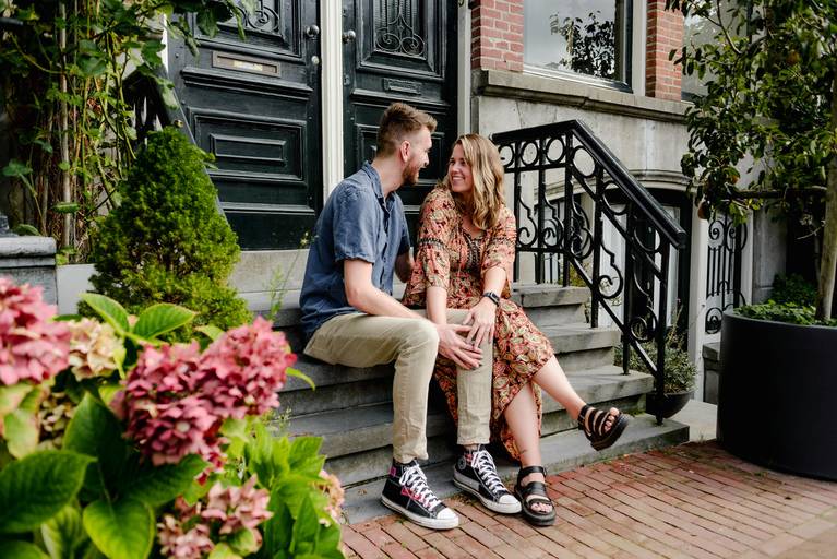Couple sitting on classic Amsterdam steps, smiling at each other during a proposal photo shoot in the canal district.