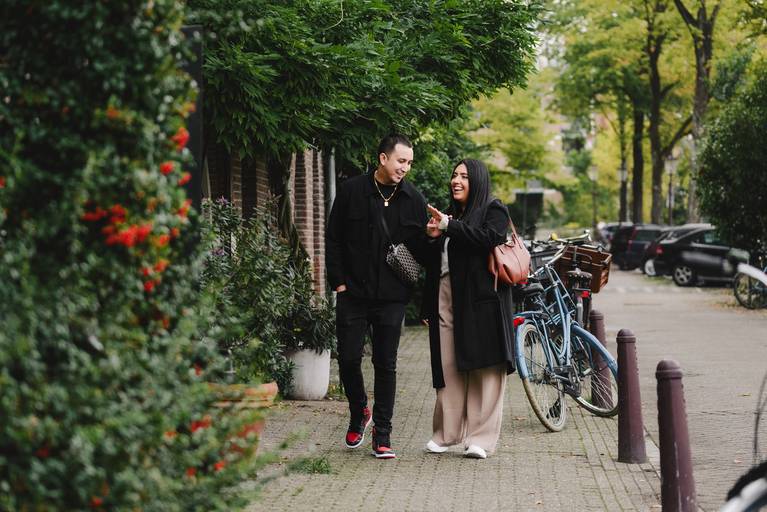 Couple walks through a quiet Amsterdam neighborhood, laughing and admiring the engagement ring during their proposal photoshoot.
