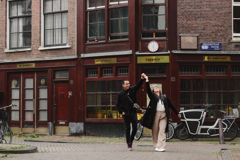Couple twirls together in a quiet Amsterdam street after their proposal, surrounded by old brick façades and local shops.