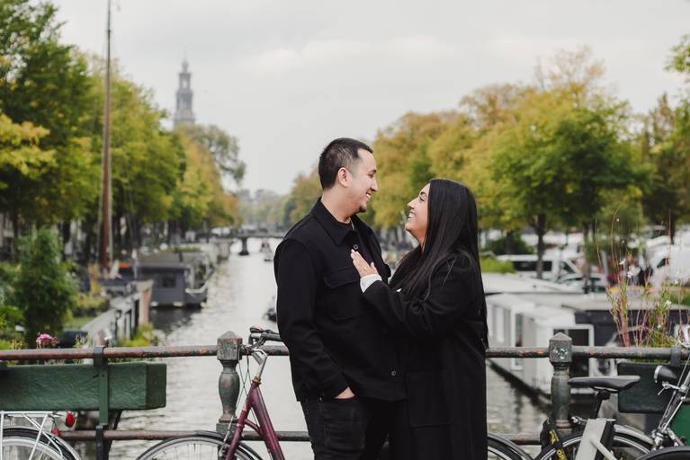 Man proposes on an Amsterdam canal bridge as his partner reacts with joy. Boats and historic houses frame the moment during a surprise engagement session in the city.