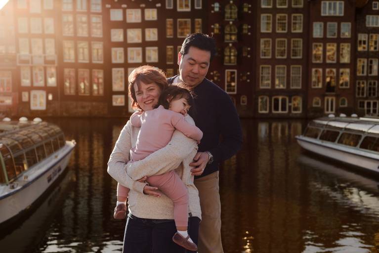 Family portrait during a vacation photography session in Amsterdam, parents holding their child by the canal at golden hour.