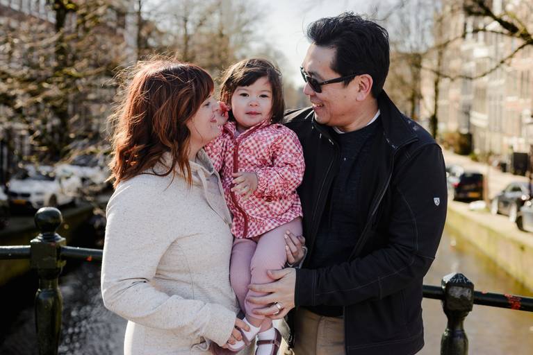 Close family moment during a vacation photo session in Amsterdam, parents holding their child on a canal bridge.