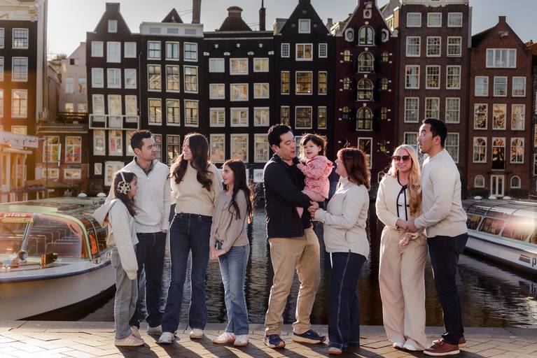 Extended family enjoying a vacation photography session by the Amsterdam canals, standing together with historic canal houses in the background.