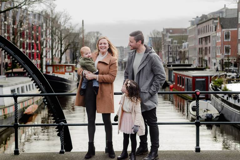Family photo session on a canal bridge in Amsterdam, parents and children smiling during a winter vacation photography session.