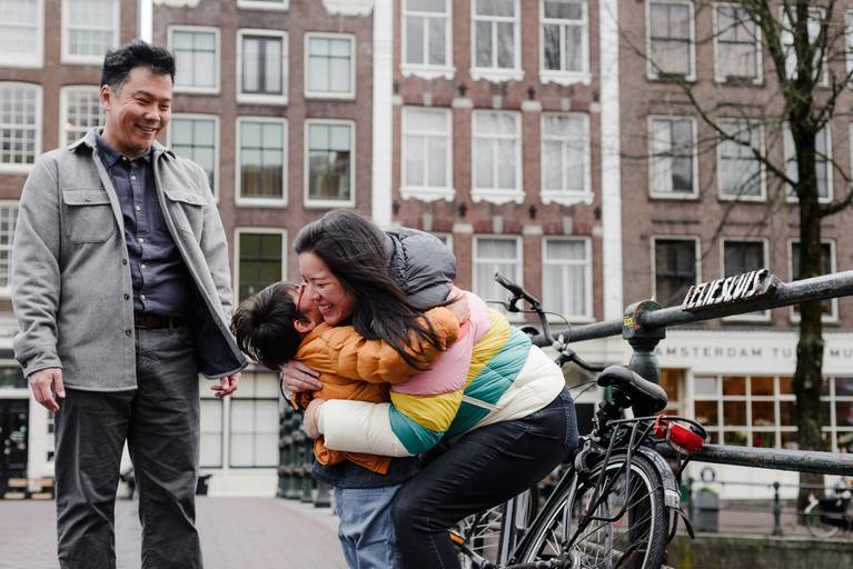 Emotional family moment during a vacation photography session in Amsterdam, parents hugging their child near a canal bridge.