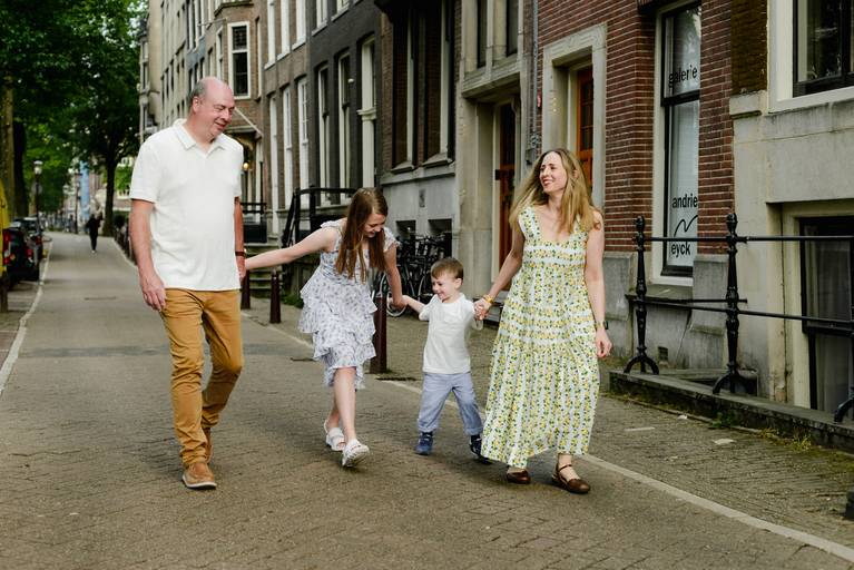 Parents and two children walking along a quiet Amsterdam street, holding hands and smiling during a family photo session.
